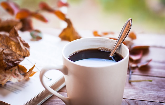 Taza de café humeante caliente y un viejo libro sobre la mesa de madera