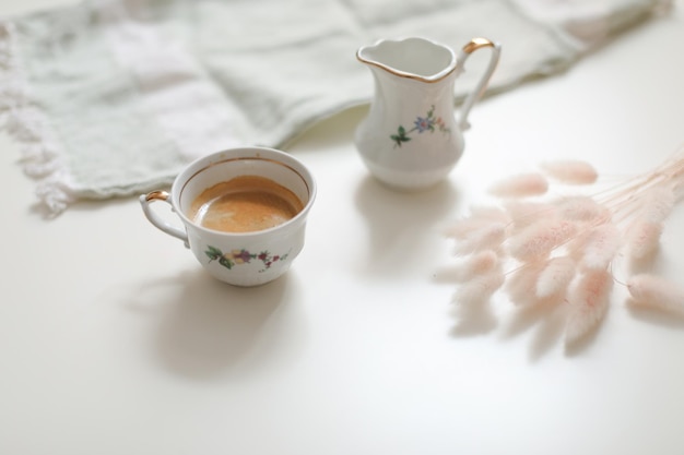 Taza con café y jarra de leche sobre un fondo blanco de madera primer plano Concepto de rutina matutina de desayuno energético