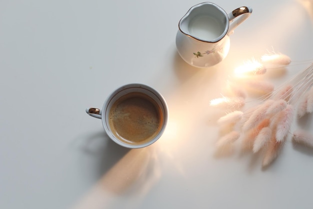 Taza con café y jarra de leche sobre un fondo blanco de madera primer plano Concepto de rutina matutina de desayuno energético