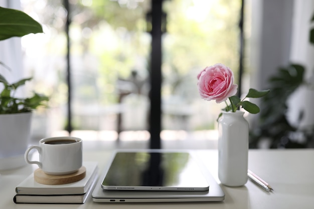 Taza de café y jarrón de rosa con tableta en mesa de madera interior