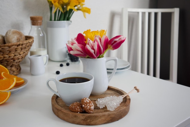 Una taza de café y un jarrón con tulipanes y narcisos sobre un soporte de madera sobre una mesa en la cocina