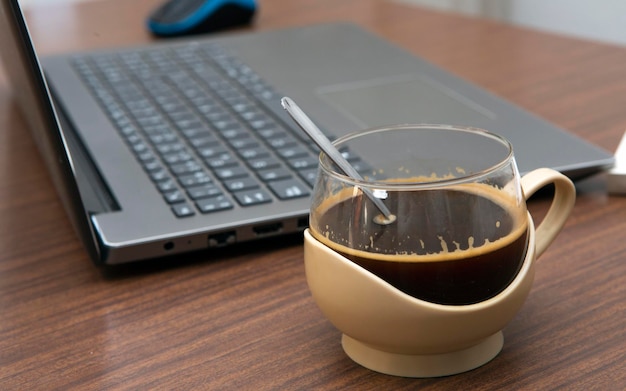 Taza de café junto a la computadora portátil en el escritorio con enfoque selectivo