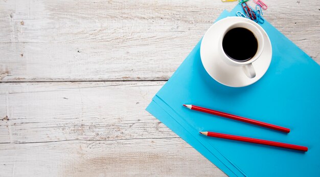 Taza de café con lápices sobre papel azul en la mesa