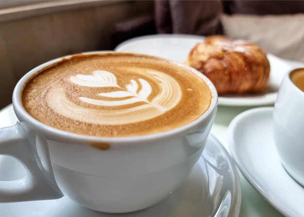 Una taza de café latte art caliente con un croissant