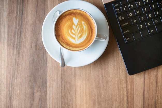 Una taza de café Latte Art con laptop en madera