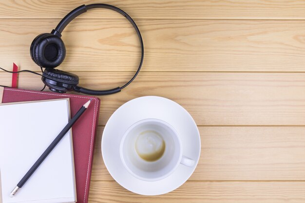 Taza de café con leche, cuaderno, lápiz y auriculares en mesa de madera