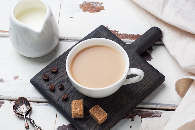 Una taza de café con leche y cubitos de caña de azúcar sobre una mesa de madera