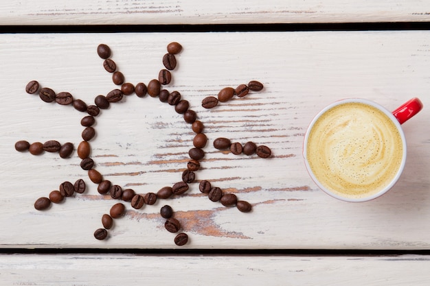 Foto taza de café con leche con espuma y sol de frijoles. madera blanca en superficie.