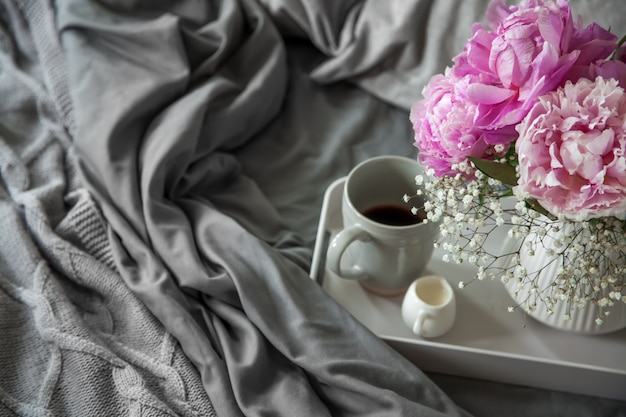 Taza de café con leche y flores en una bandeja en la cama