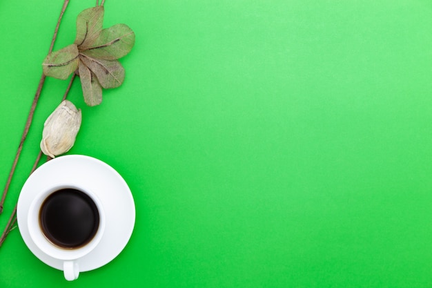 Taza de café con leche con flores de papel sobre fondo de papel verde.