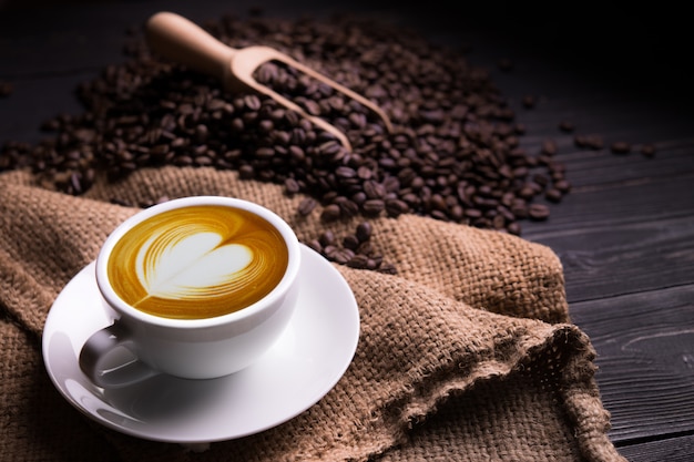 Taza de café con leche con forma de corazón y granos de café sobre fondo de madera vieja