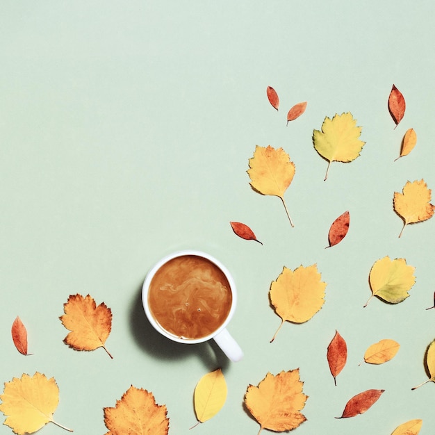 Taza de café con leche y hojas de otoño amarillas rojas sobre composición de otoño verde pastel