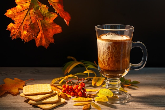 Taza de café con leche junto al otoño de hojas de serbal y galletas