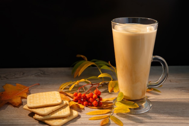 Taza de café con leche junto al otoño de hojas de serbal y galletas