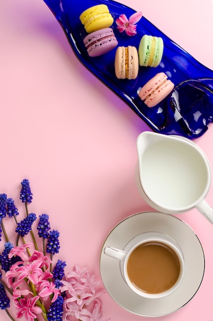 Taza de café con leche, macarrones y tarro de leche en rosa pastel