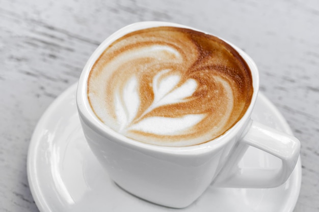 Una taza de café con leche en la mesa de madera blanca