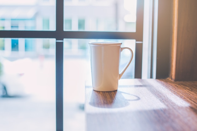 Taza de café con leche en la mesa de madera junto a la ventana.