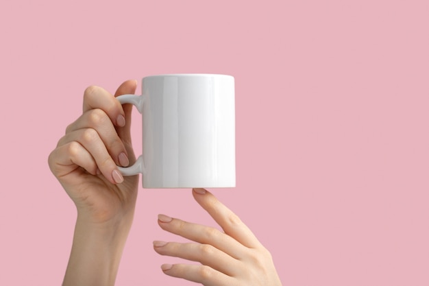 Taza de café con leche o taza en manos femeninas en rosa