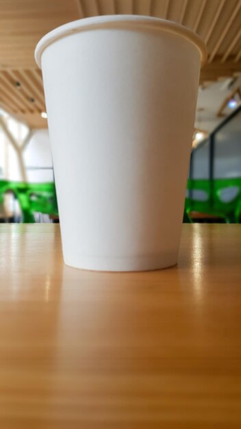 Taza de café con leche de papel desechable para llevar o llevar, en la mesa de madera de la cafetería o comedor, lugar para un diseño de diseño. Taza de café caliente en un café.