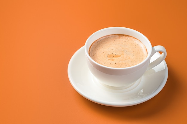 Taza de café con leche en la pared naranja con espacio de copia. Vista lateral.