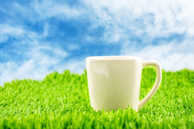 Taza de café con leche en pasto verde con cielo azul, temporada de primavera