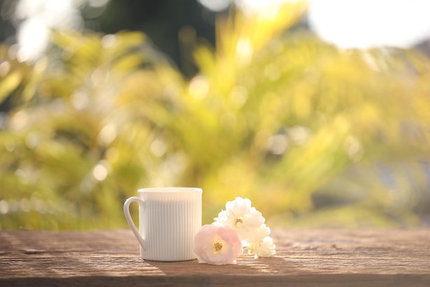 Taza de café con leche y rosas en la mesa de madera al aire libre