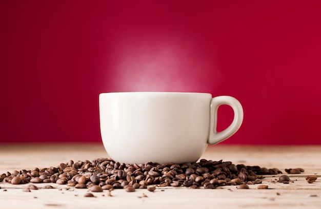 Taza de café con leche rota con humo de vapor caliente y frijoles en la mesa de madera con fondo rojo.