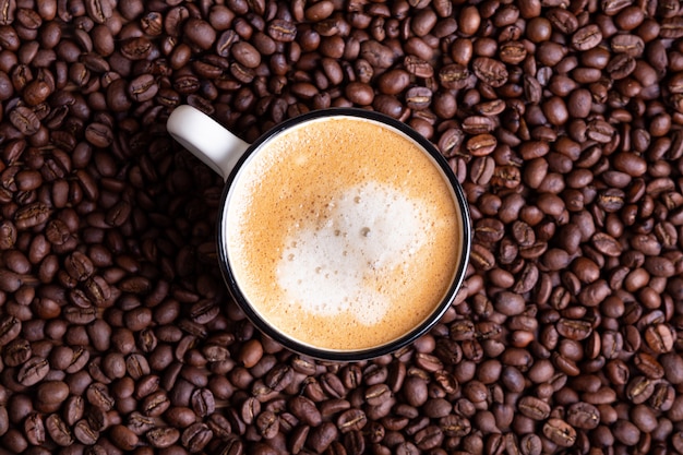 Taza de café con leche sobre un fondo oscuro sólido de granos de café tostado.