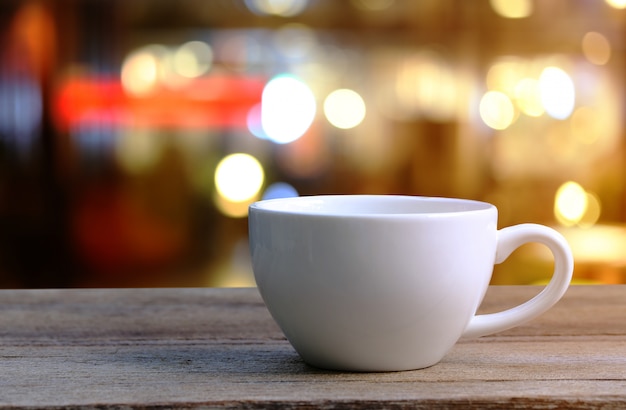 Taza del café con leche en la tabla de madera en fondo de la falta de definición de la cafetería.