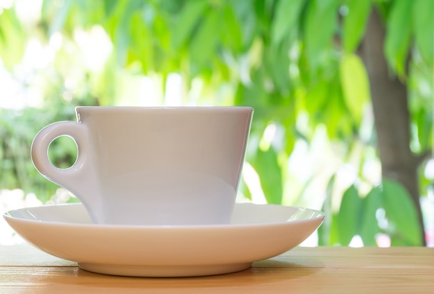 Foto taza del café con leche en la tabla de madera en el fondo tropical del jardín.