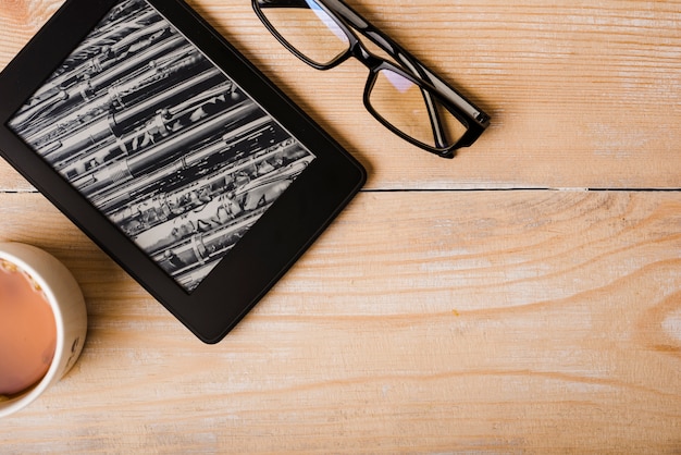 Foto taza de café; lentes y lector de libros electrónicos en el escritorio de madera.