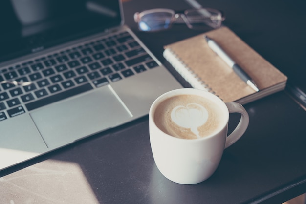 Taza de café lette y cuaderno con una pluma en la mesa de madera