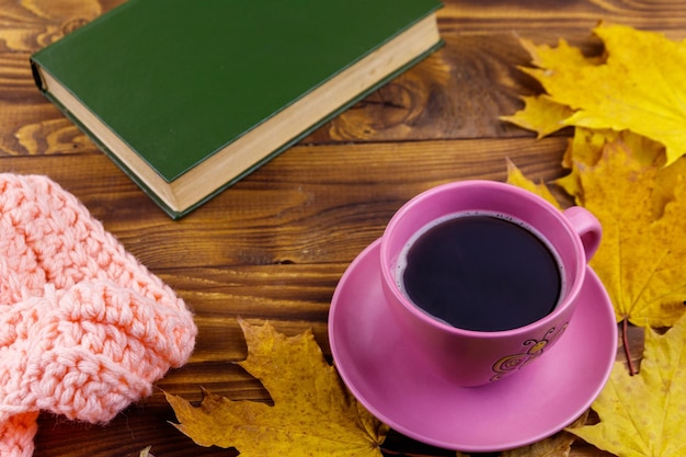 Taza de café libro bufanda tejida y hojas de arce amarillas sobre mesa de madera Bodegón de otoño