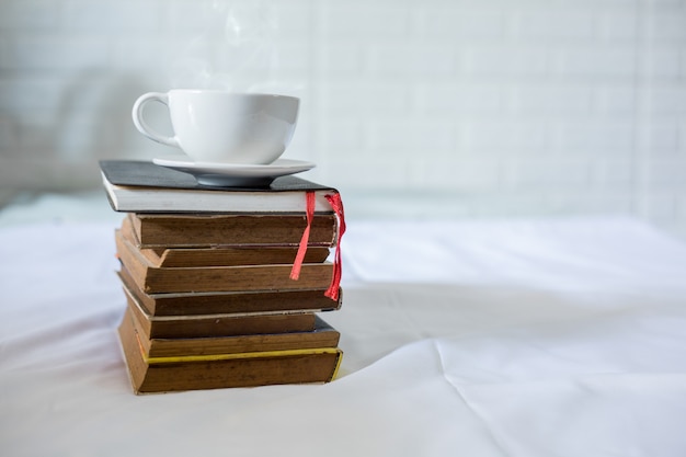 Taza de café y un libro en una cama. Taza blanca con café en un libro. De cerca