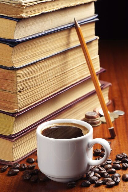 Taza de café, libros antiguos, lápiz y monedas en la mesa