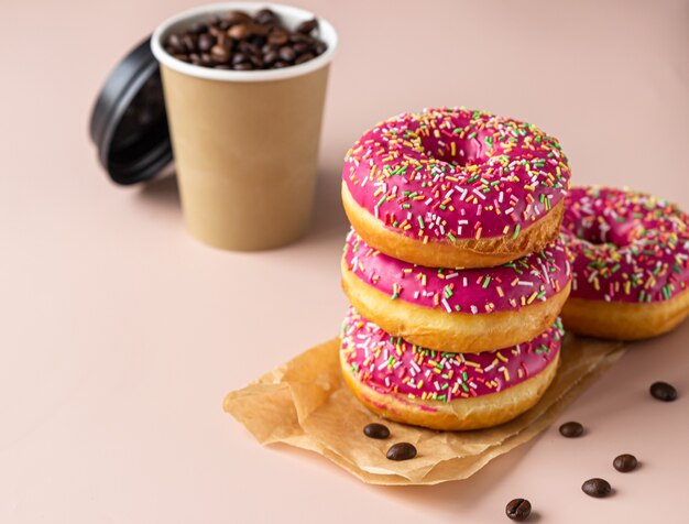 Taza de café para llevar con granos de café y postre glaseado rosa con chispitas de colores.