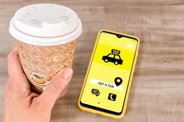 Taza de café para llevar y teléfono inteligente con aplicación en escritorio de madera Obtener aplicación de taxi