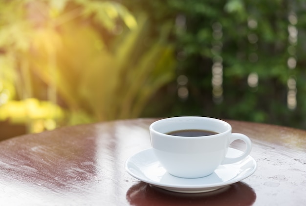 Taza de café en la luz del sol de la mañana con fondo verde jardín