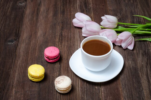 Taza de café, macarons y tulipanes rosados sobre fondo de madera. Vista superior