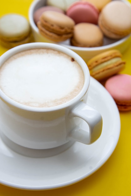 Taza de café y macarrones en colorfu mesa amarilla.