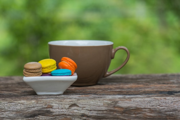 Taza de café y macarrones coloridos en plato sobre mesa de madera