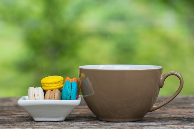 Taza de café y macarrones coloridos en plato sobre mesa de madera
