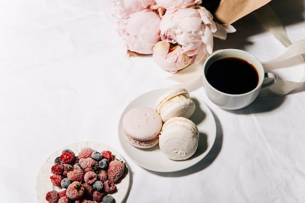 una taza de café, macarrones y flores de peonía en la cama