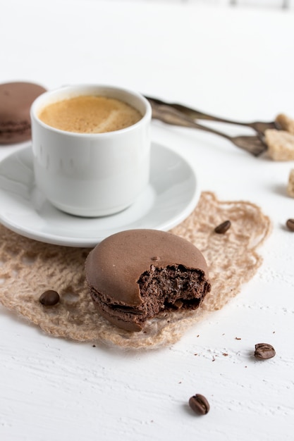 Taza de café y macarrones franceses de chocolate sobre un respaldo de madera blanca