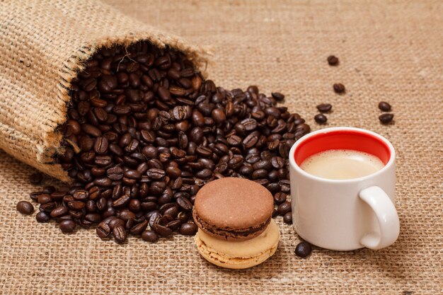 Taza de café, macarrones y granos de café tostados en un saco de lona sobre cilicio.