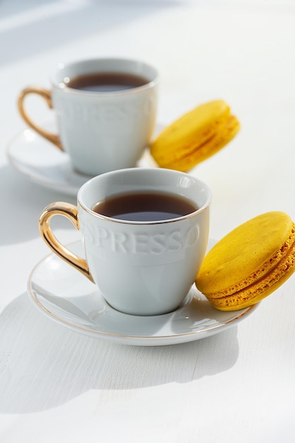 Taza de café y macarrones en mesa de madera blanca