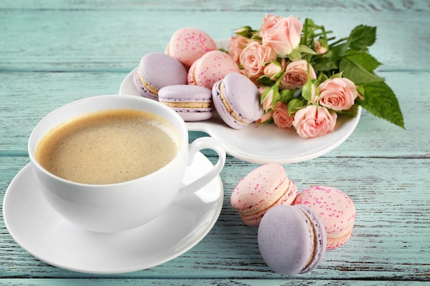 Taza de café con macarrones y rosas en la mesa de madera