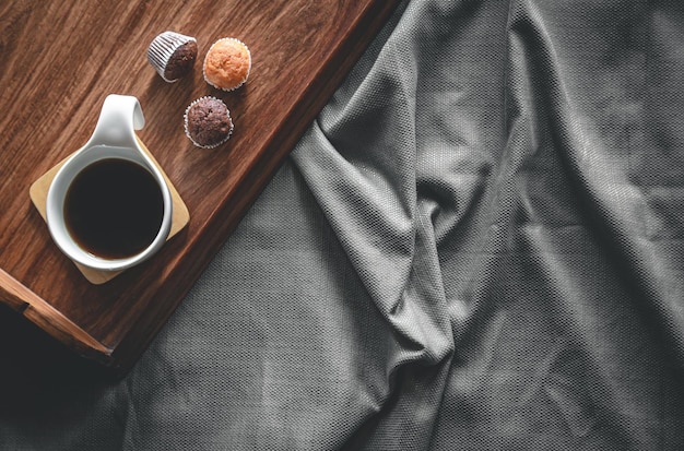 Taza de café y magdalenas en una bandeja en la cama, desayuno plano en la cama