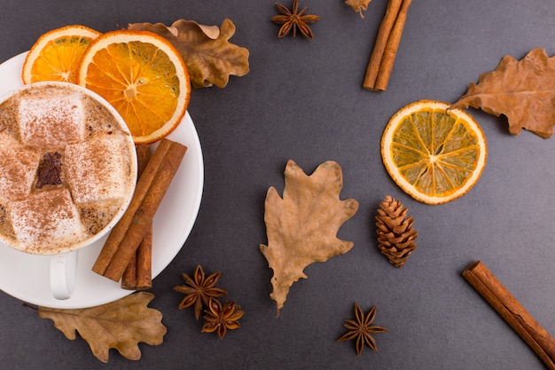 Taza de café con malvaviscos y cacao, hojas, naranjas secas, canela y anís estrellado, fondo de piedra gris. Sabrosa bebida caliente de otoño. copyspace