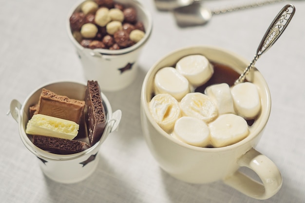 Una taza de café con malvaviscos y chocolate sobre un fondo blanco.